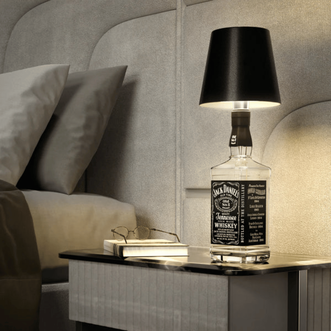 A lamp with a black shade placed on a bottle which appears to be a whiskey bottle with a label.