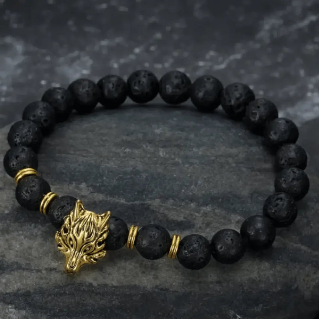 A black lava bead bracelet with a silver wolf head charm, displayed on a dark textured surface.