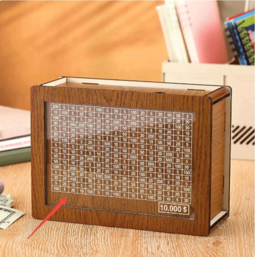 A wooden GoalBox 10K savings tracker with a progress chart and a marker, placed on a table.