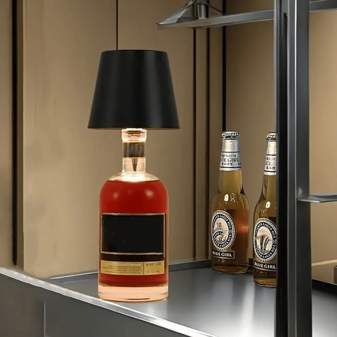 A lamp with a black shade placed on a bottle which appears to be a whiskey bottle with a label.
