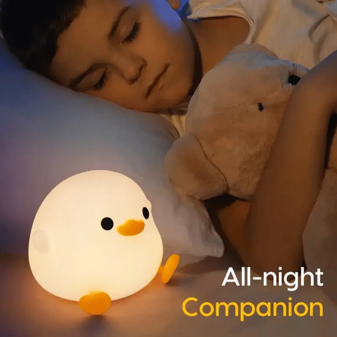 A cute, illuminated duck-shaped night light glowing with a warm light, placed on a cozy knit fabric.