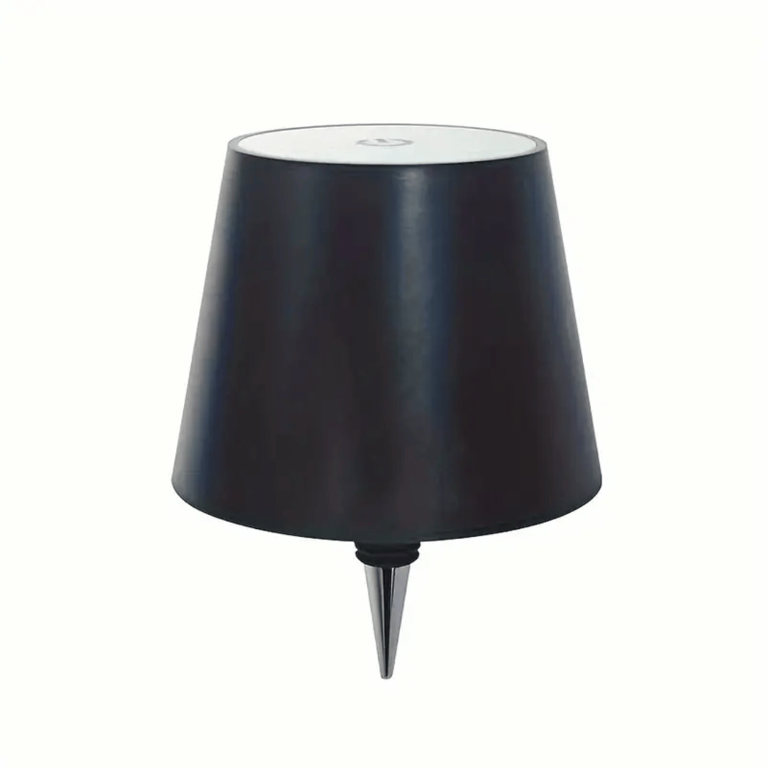 A lamp with a black shade placed on a bottle which appears to be a whiskey bottle with a label.