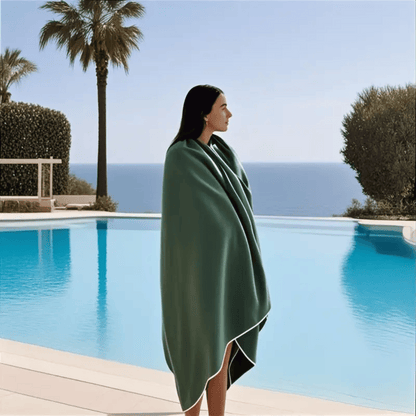 Person wrapped in a green towel by a pool with ocean views.