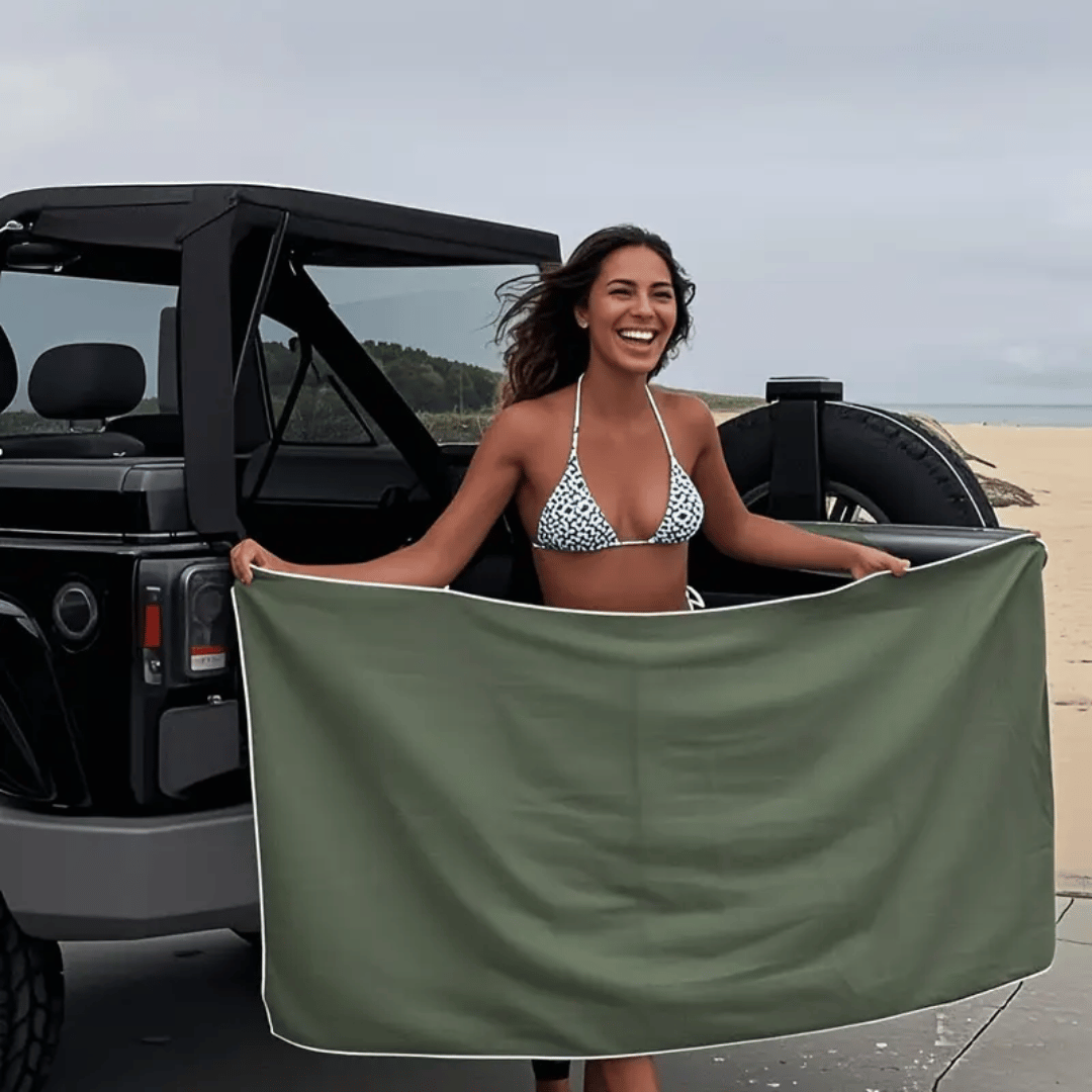 Woman holding a green towel at a beach with a black jeep.