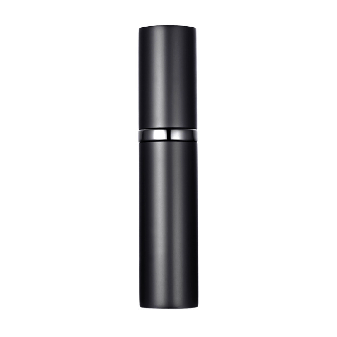 A hand holding a black travel-size perfume atomizer with a fine spray of perfume, highlighting the product's capability to spray without water drops.