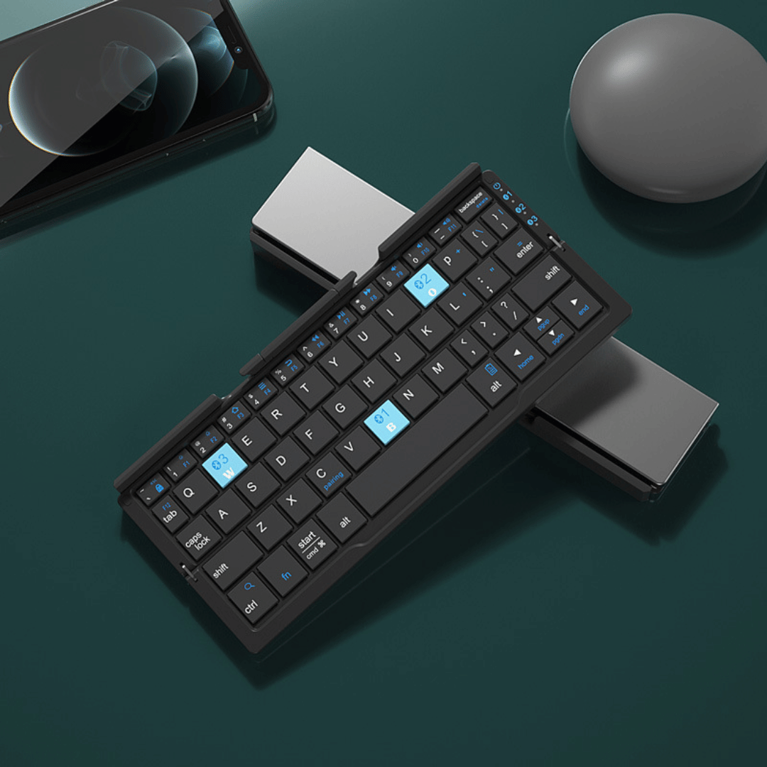Foldable keyboard on a dark surface with a phone, mouse, and pen in the background.