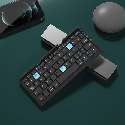 Foldable keyboard on a dark surface with a phone, mouse, and pen in the background.