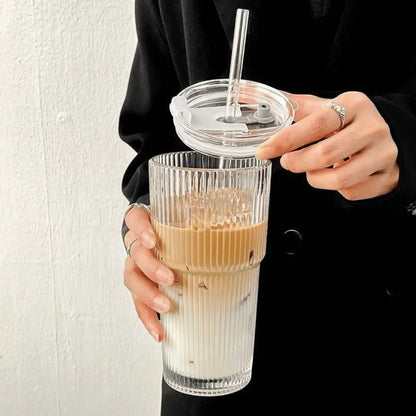 Person holding a clear glass with layered drink and straw lid against a plain background
