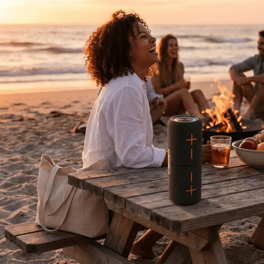 Person sitting at a picnic table on the beach with a portable speaker and sunset in the background