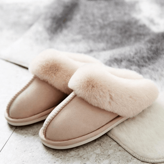 Pair of beige slippers with fur trim on a light surface