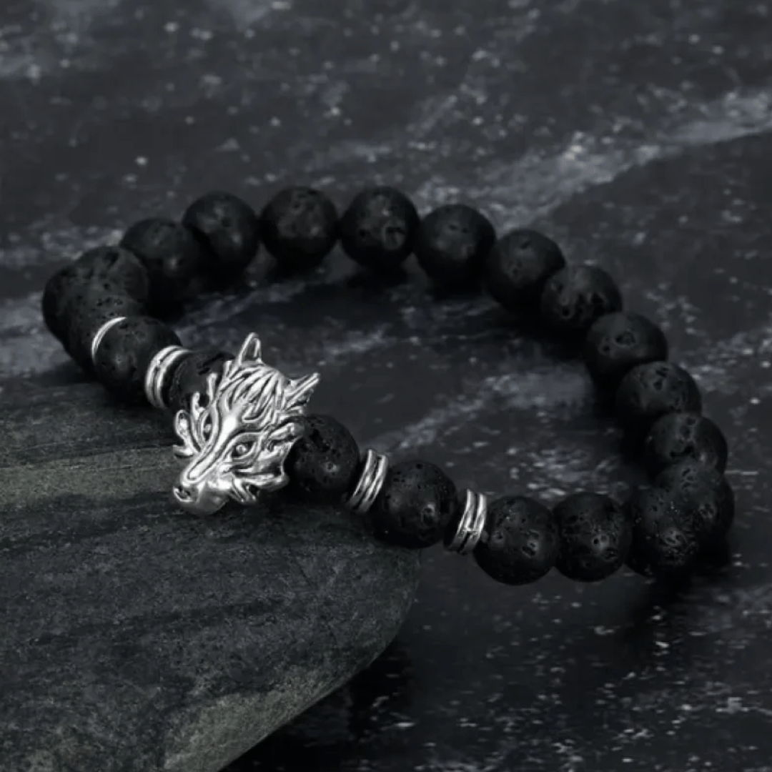 A black lava bead bracelet with a silver wolf head charm, displayed on a dark textured surface.