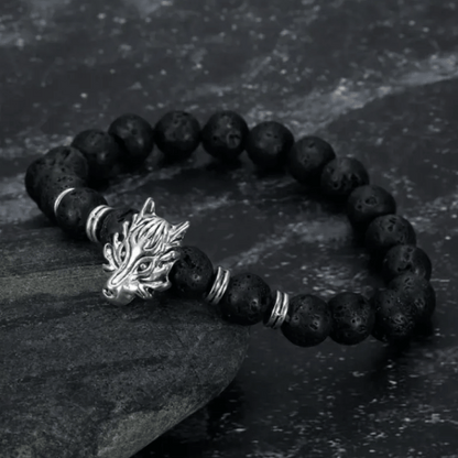 A black lava bead bracelet with a silver wolf head charm, displayed on a dark textured surface.