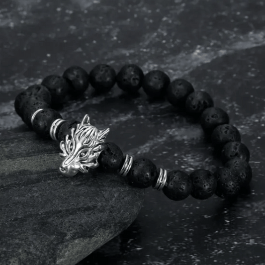 A black lava bead bracelet with a silver wolf head charm, displayed on a dark textured surface.