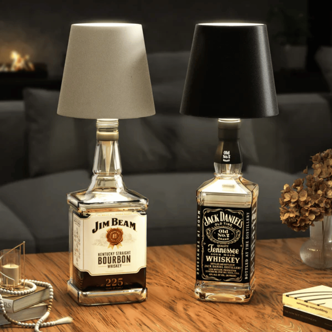 A lamp with a black shade placed on a bottle which appears to be a whiskey bottle with a label.