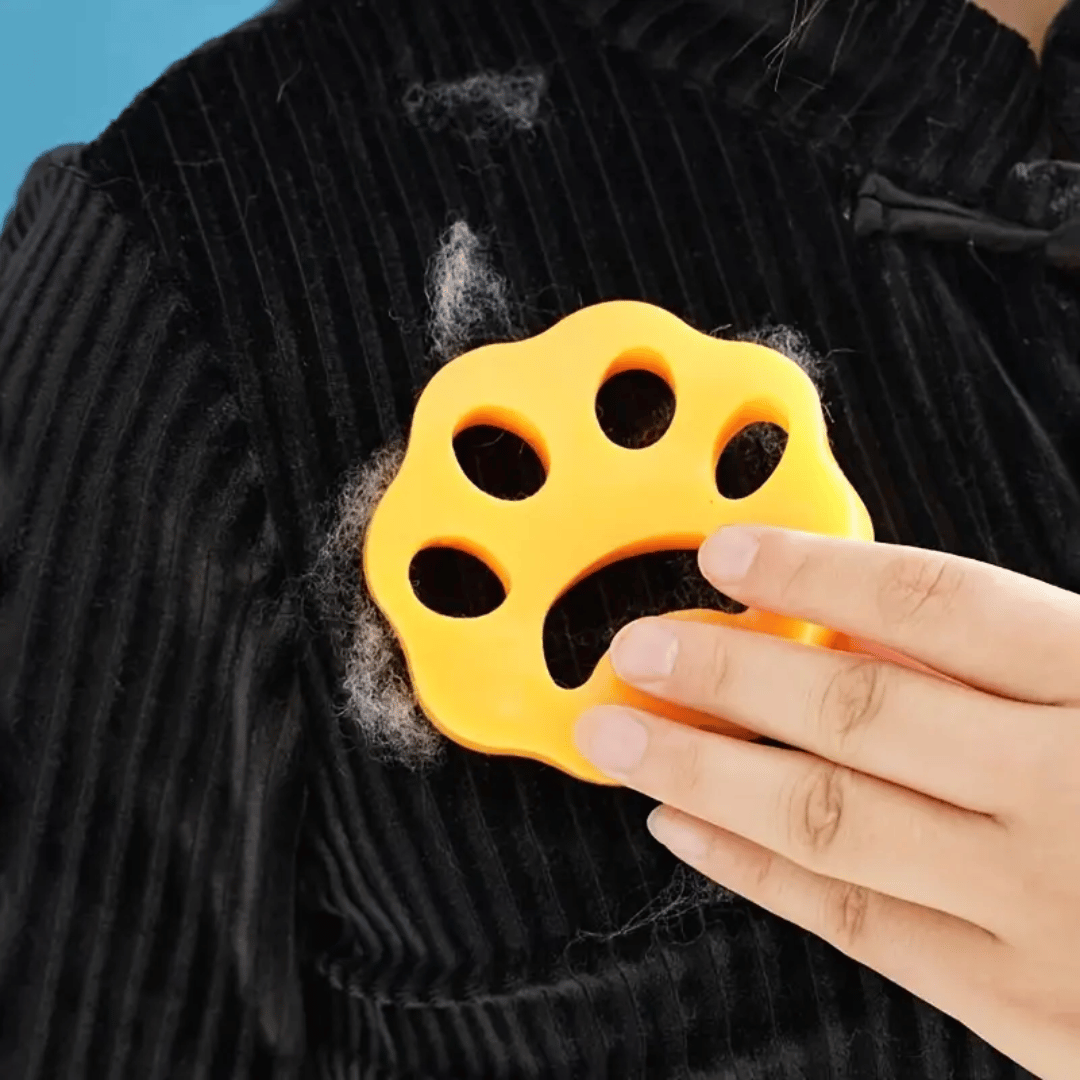 Yellow paw-shaped pet grooming tool being used on a black fabric surface with fur.