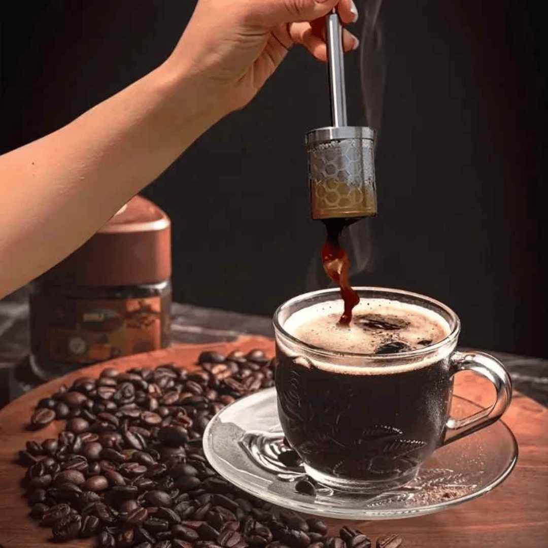 A stainless steel AromaPress lying on a bed of coffee beans, suggesting a connection to coffee brewing.