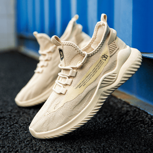 A pair of beige VYRON sneakers with a textured upper and a unique sole design, placed against an urban backdrop.