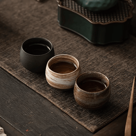 A collection of ceramic cups, likely used for tea or coffee, displayed on a table. They have a textured surface and come in various shades of brown and beige.
