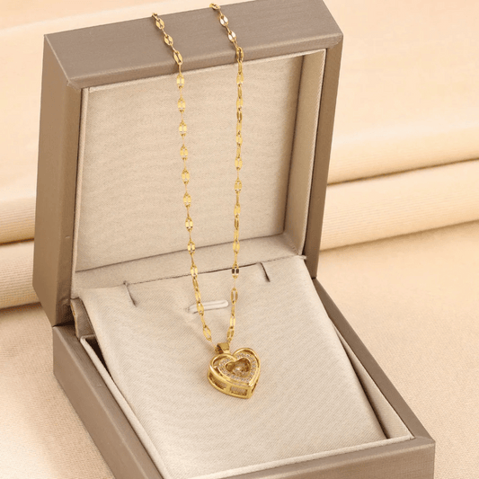 A gold heart pendant necklace presented in a gray box with a white cushion.