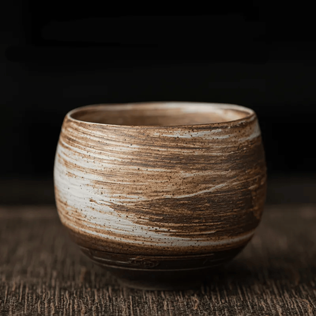 A collection of ceramic cups, likely used for tea or coffee, displayed on a table. They have a textured surface and come in various shades of brown and beige.