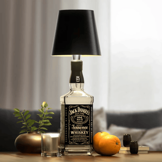 A lamp with a black shade placed on a bottle which appears to be a whiskey bottle with a label.