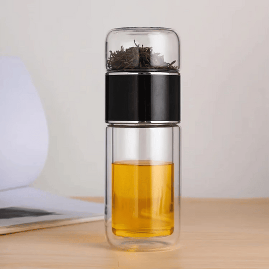 A sleek, double-walled glass tea infuser bottle with a black lid, shown with tea leaves on the top chamber and liquid in the bottom chamber.