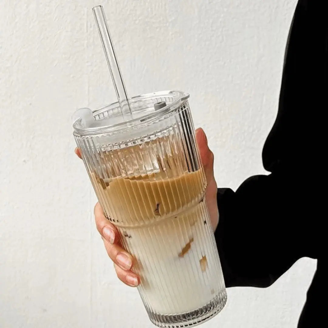 Hand holding a clear iced coffee drink with a straw against a light background