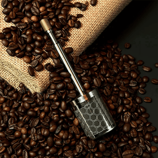 A stainless steel AromaPress lying on a bed of coffee beans, suggesting a connection to coffee brewing.