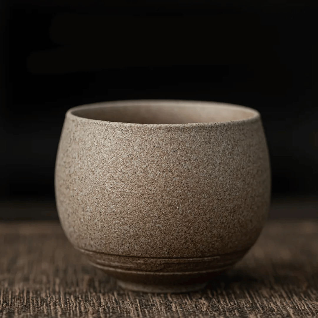 A collection of ceramic cups, likely used for tea or coffee, displayed on a table. They have a textured surface and come in various shades of brown and beige.