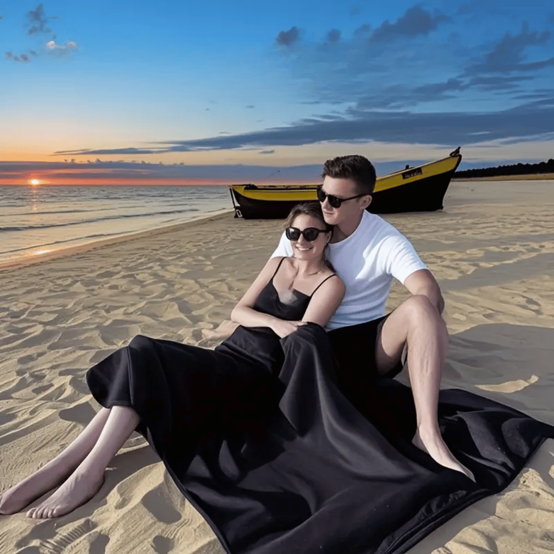 Couple sitting on a beach at sunset with a boat in the background.