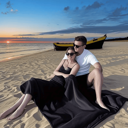 Couple sitting on a beach at sunset with a boat in the background.