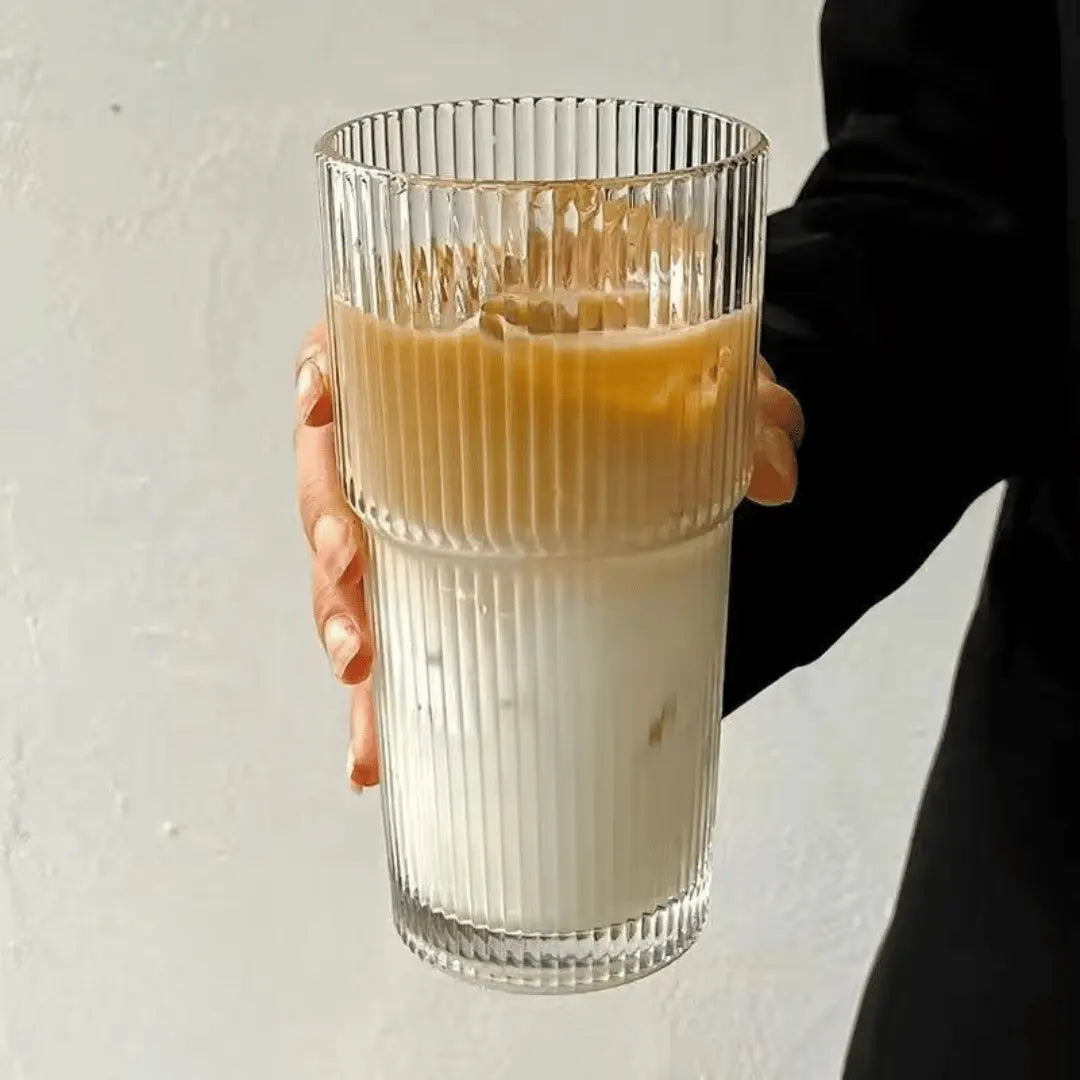 Hand holding a glass of layered iced coffee and milk against a neutral background