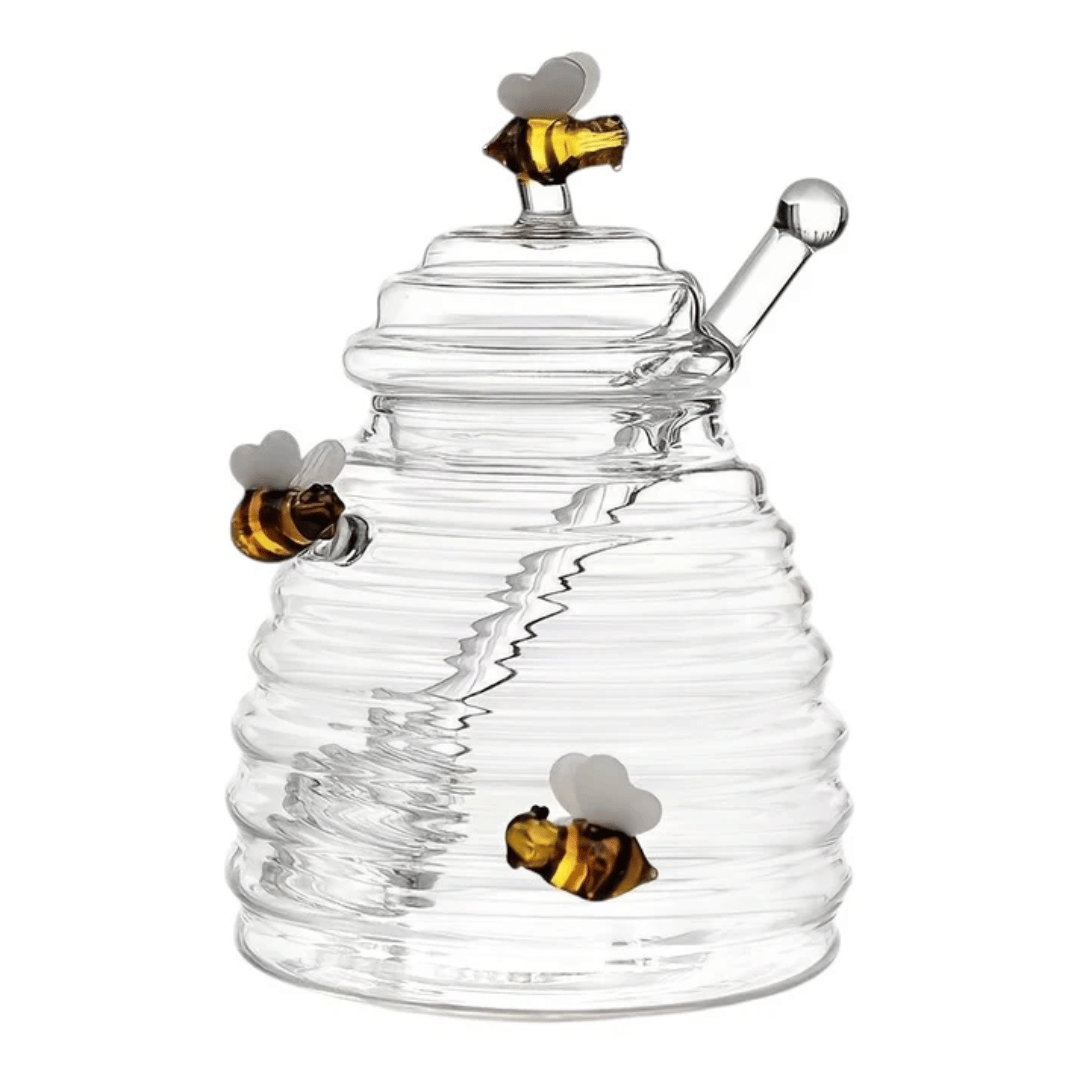 A person is pouring liquid from a clear glass jar with a honeycomb pattern into another container, using a metal honey dipper.