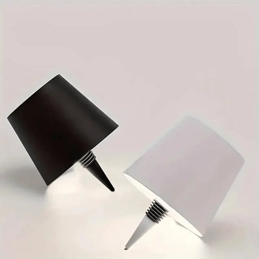 A lamp with a black shade placed on a bottle which appears to be a whiskey bottle with a label.