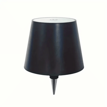 A lamp with a black shade placed on a bottle which appears to be a whiskey bottle with a label.