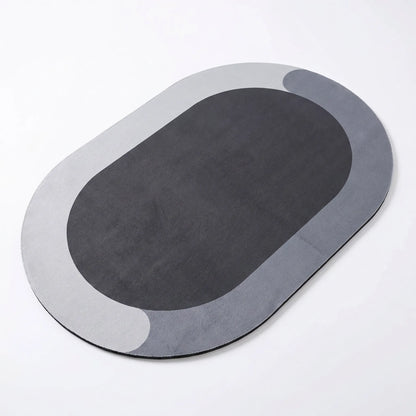 A gray oval-shaped bathroom mat placed on a tiled floor, with a pair of slippers at the top right corner.